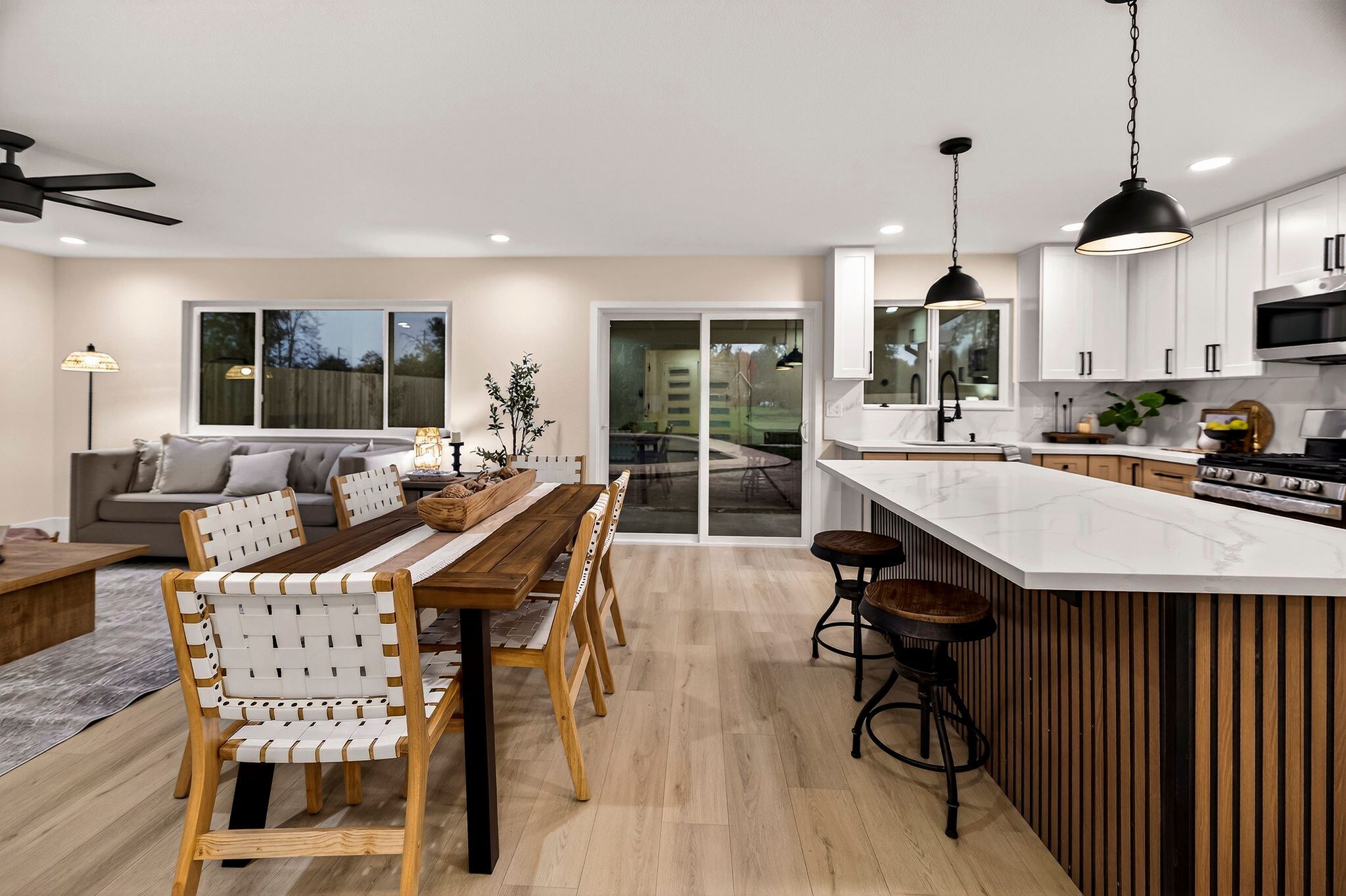 Remodeled open great room with living area, dining table and white shaker kitchen